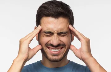 homem com as duas mãos na cabeça representando dor do bruxismo
